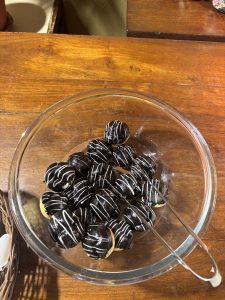 A clear glass bowl filled with round chocolate treats drizzled with white chocolate, resting on a wooden surface.