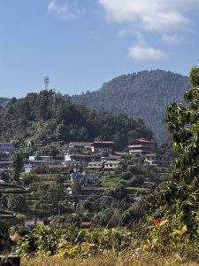 A serene mountainous landscape featuring a hillside village with various houses, some with red roofs, interspersed with greenery.
