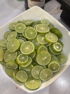 A white square bowl filled with numerous sliced limes, showing their bright green flesh and some seeds.