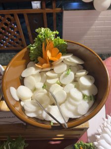 A brown bowl filled with circular slices of white radish and scattered green lettuce leaves.