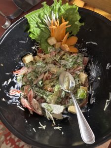 A large black bowl filled with a colorful salad consisting of fresh lettuce, sliced tomatoes, croutons, and a creamy dressing. 
